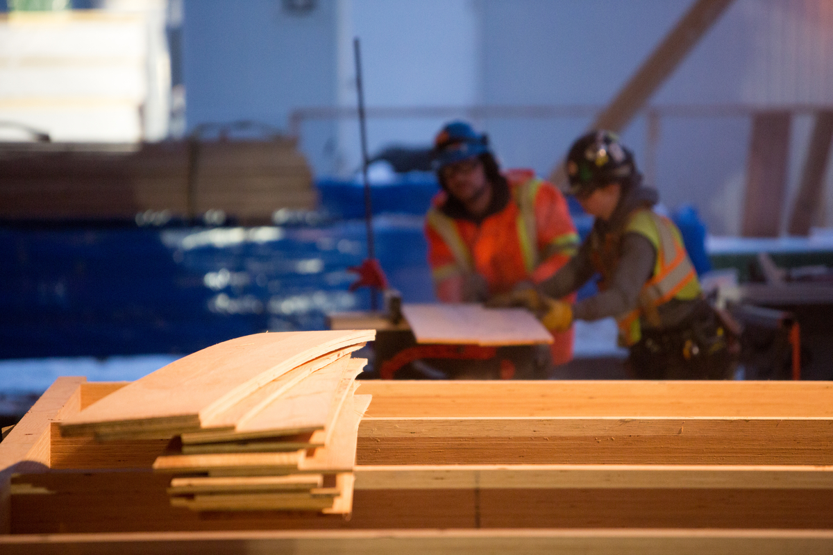 堆叠完成的层压板条，背景是工人在这个大规模木结构施工现场，展示了轻框架木材和大规模木结构施工和设计的价值、多功能性和灵活性
