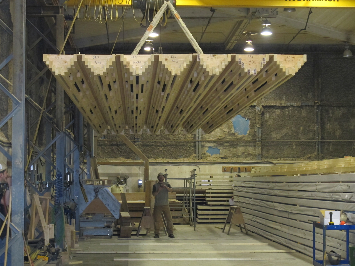 预制木材面板由桥式起重机悬挂，作为大木材厂施工过程的一部分。预制木材面板由桥式起重机悬挂，作为大木材厂施工过程的一部分