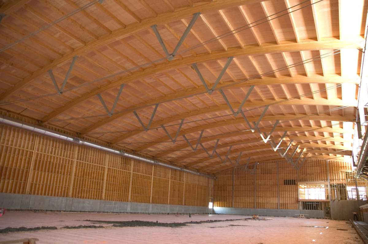 Armstrong-Spallumcheen竞技场的日间室内景观，显示拱形胶合层压梁，木桁架和胶合板屋顶上方，预制木面板墙下方