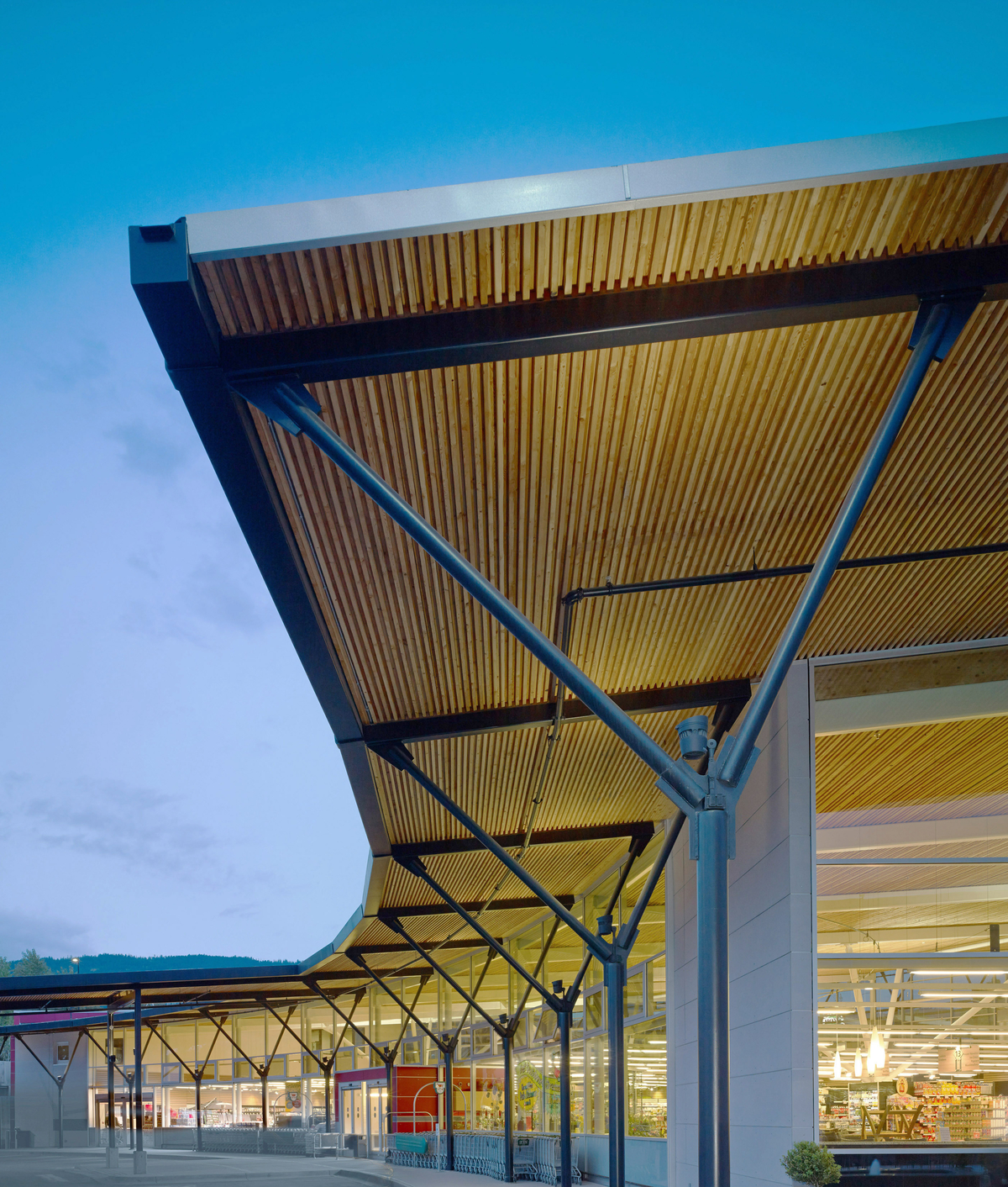 Askews超市正面的室外傍晚视图，展示了钉层压木材(NLT)和钢的覆盖混合走道，沿着两层低层玻璃店面运行