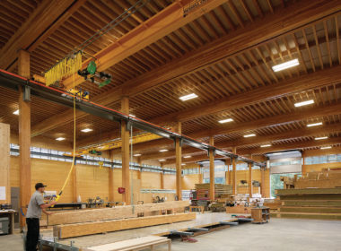 BC被动式房屋工厂的内部视图显示工人使用起重机移动大量的木梁