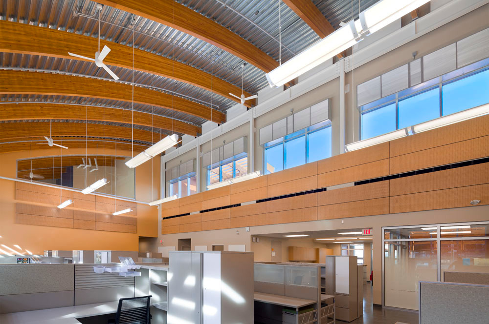 位于BC Maple Ridge的BC水电维护和运营设施的日间室内视图，显示办公室和工作空间，木质镶板和装饰由弯曲的胶合木(胶合木)木屋顶梁保护，顶部是金属覆盖的外屋顶表面