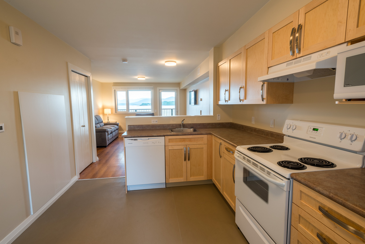 模块化被动式房屋/高性能Bella Bella员工住房的室内白天视图，展示白色漆木装饰，自然棕褐色厨房橱柜和当代设计特色
