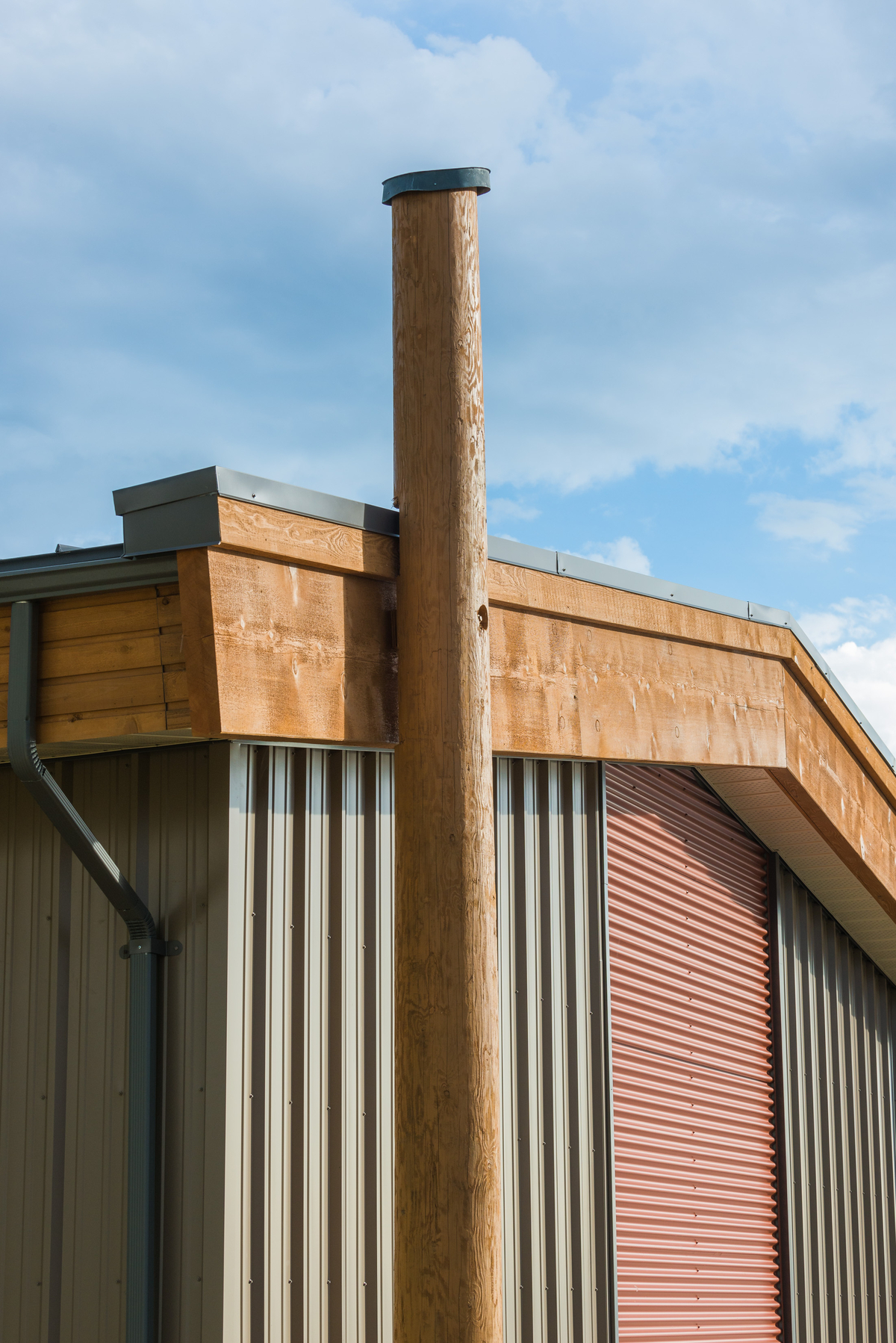 模块化被动式房屋/高性能贝拉贝拉员工住房的外部下午视图，展示了垂直原木杆和钢筋和实锯重木材建筑的侧面