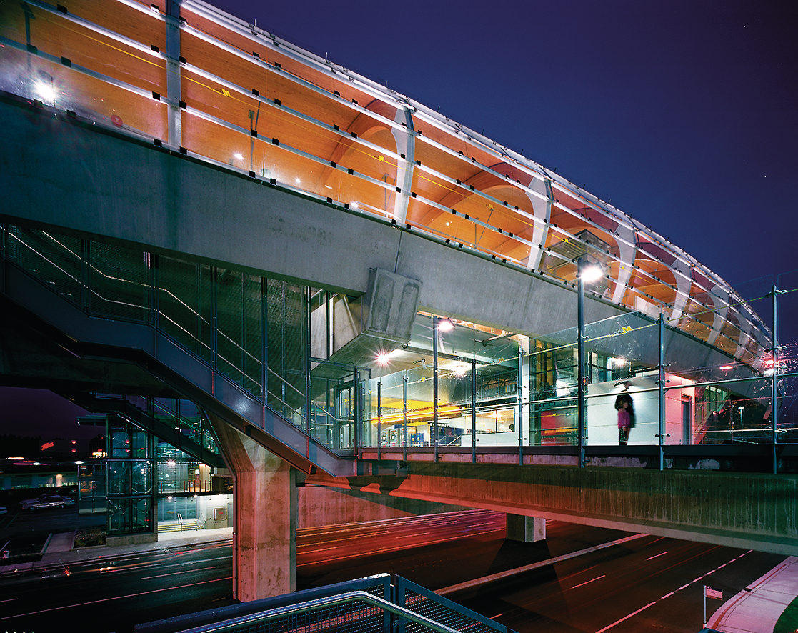 弯曲的玻璃外面板和支撑木制天花板的大型拱形钉层压木材(NLT)梁是本纳比市布伦特伍德镇中心中转站的艺术夜景的突出特征