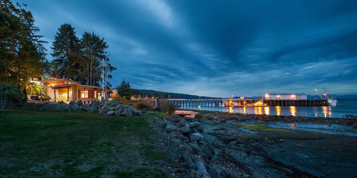 加拿大海岸警卫队搜索和救援站的外部远处夜景，显示海岸线，岩石，水，码头，和车站本身的外部木墙板，柱子和梁，和木装饰