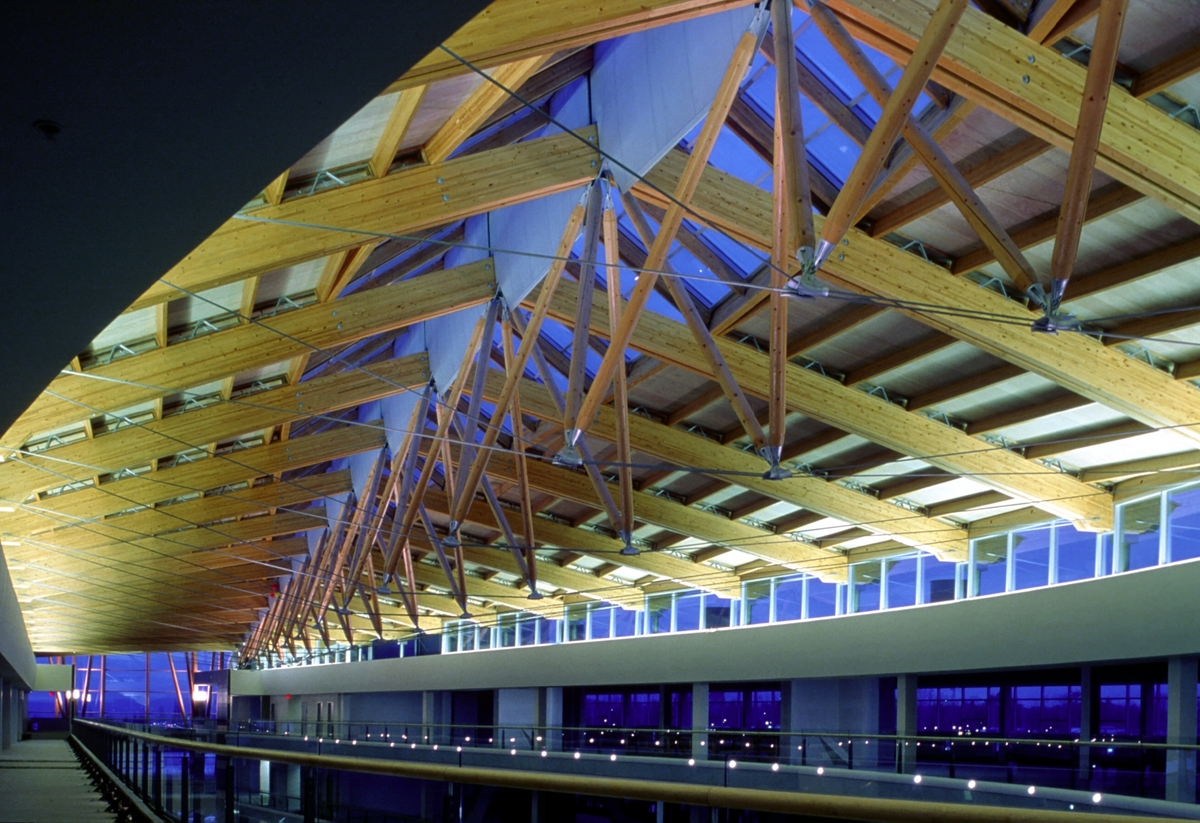 萨里中心城市天花板结构的室内夜景，显示钢张拉索，胶合层压木材(胶合木)梁，中央玻璃和木脊
