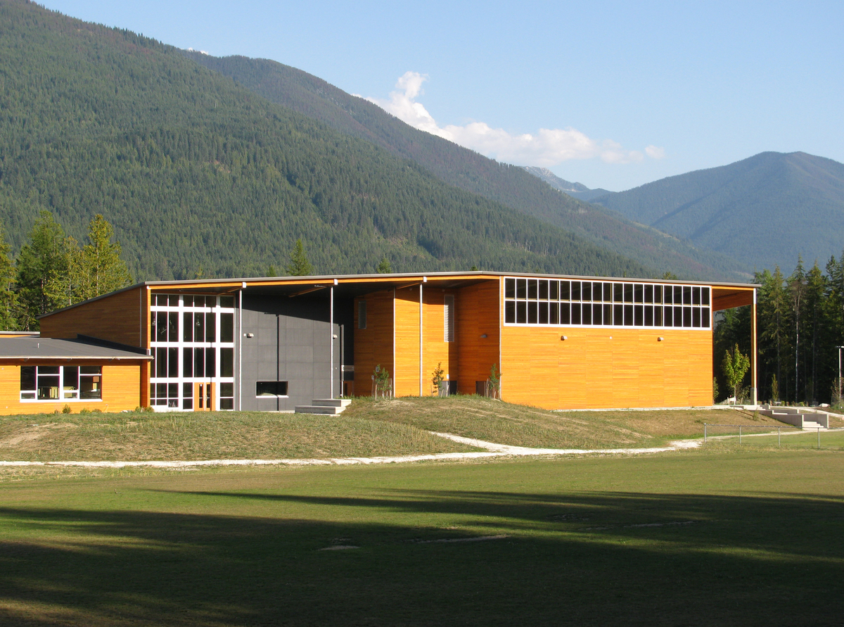 克劳福德湾小学(Crawford Bay Elementary-Secondary School)低层建筑的外部全景，展示了金属和木材混合结构，有木镶板、柱子+梁，以及由堆叠的木板和胶合梁在现场预制的屋顶悬垂