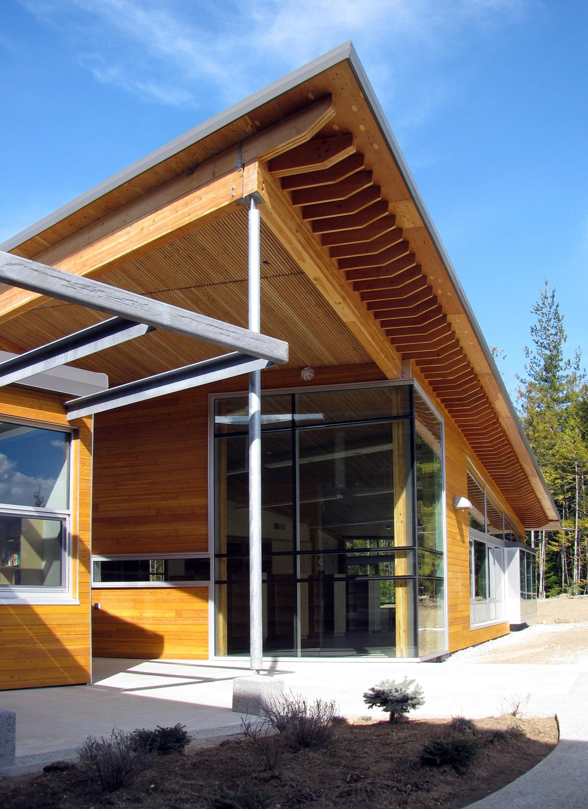 克劳福德湾小学(Crawford Bay Elementary-Secondary School)低层建筑的外景，展示了混合建筑与显著的木材使用，包括镶板、柱子+梁，以及由堆叠的木板和胶合木梁在现场预制的屋顶悬垂