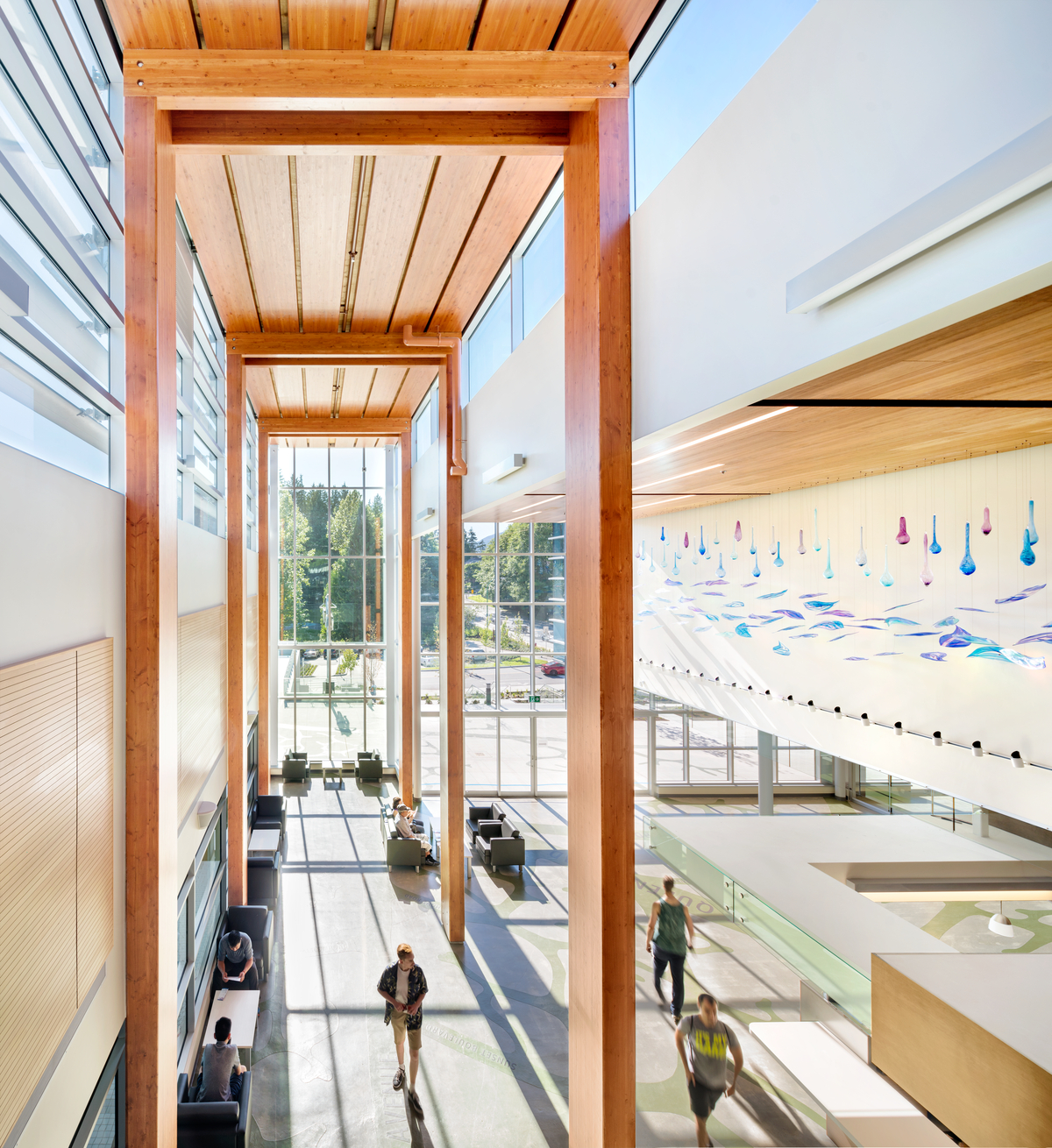 德尔布鲁克社区娱乐中心主大厅内的室内阳光白天视图，该中心具有全玻璃正面和全高胶合层压木材(胶合木)柱和梁支撑木质建筑“脊柱”