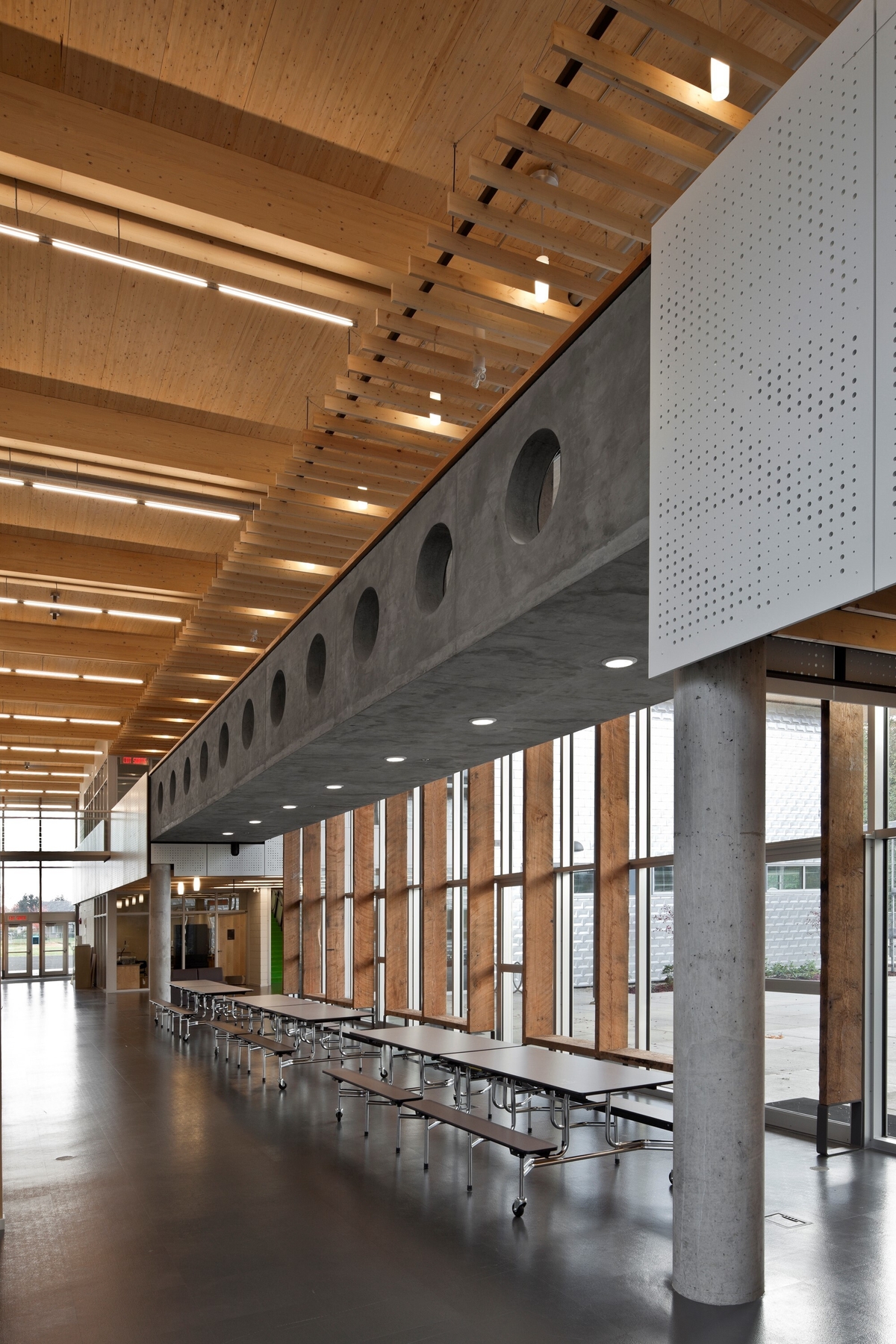 低层建筑École au - ceau -de-l ' île小学两层主入口大厅和办公室的日间景观，展示了暴露的道格拉斯冷杉木材，胶合木(胶合木)屋顶梁，2楼混凝土走道和广泛的木材装饰