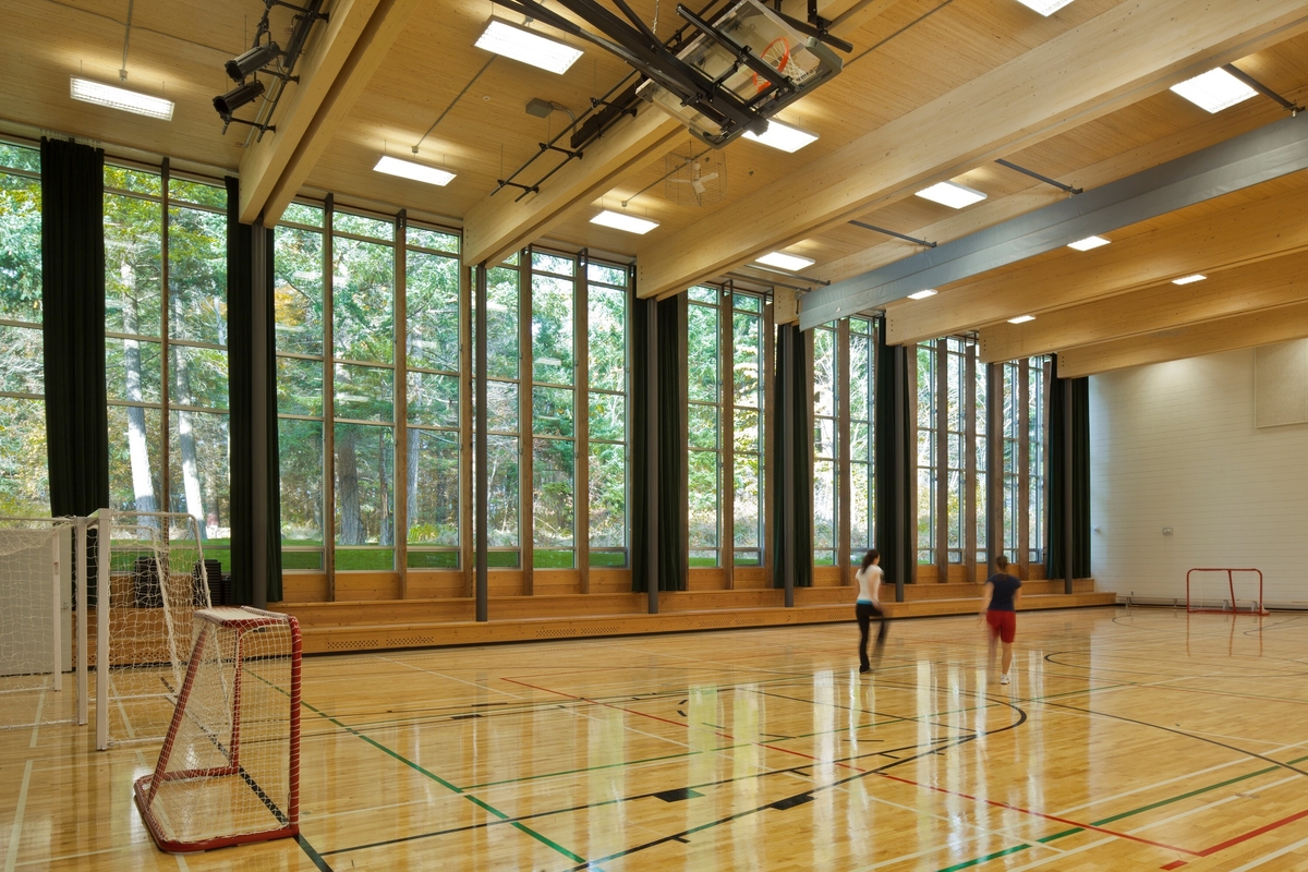 阳光明媚的白天，École Mer-et-Montagne体育馆的室内景观，展示了整个外部玻璃墙，暴露的道格拉斯冷杉天花板梁木材支撑CLT天花板部分，所有以上都是木制多功能地板，由2名学生占用