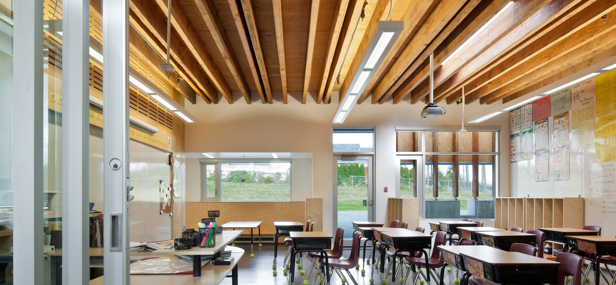 低层建筑École Mer-et-Montagne小学教室的室内日间景观，展示了暴露的道格拉斯冷杉木材和木材口音