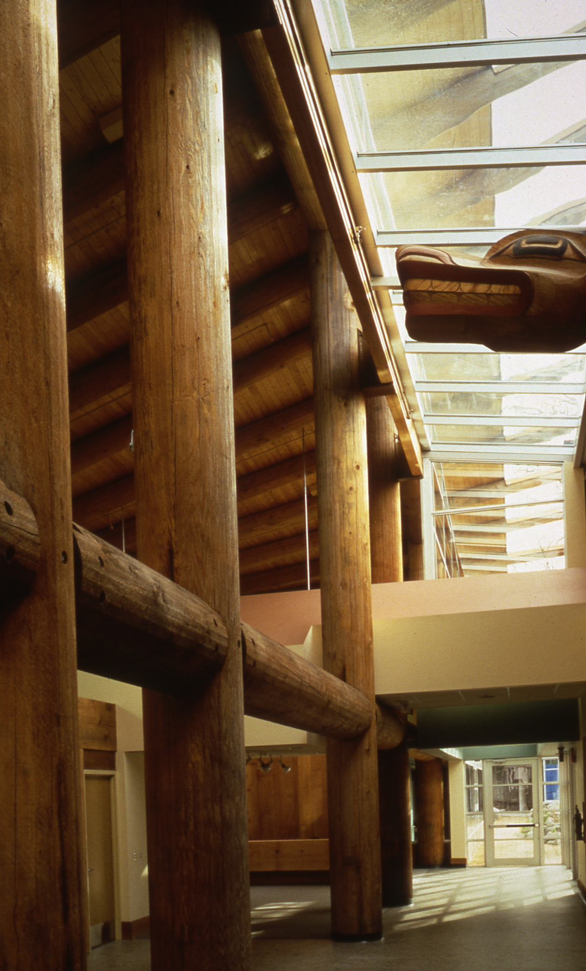 英属哥伦比亚大学第一民族长屋的日间室内图像，展示了巨大的木杆梁和柱