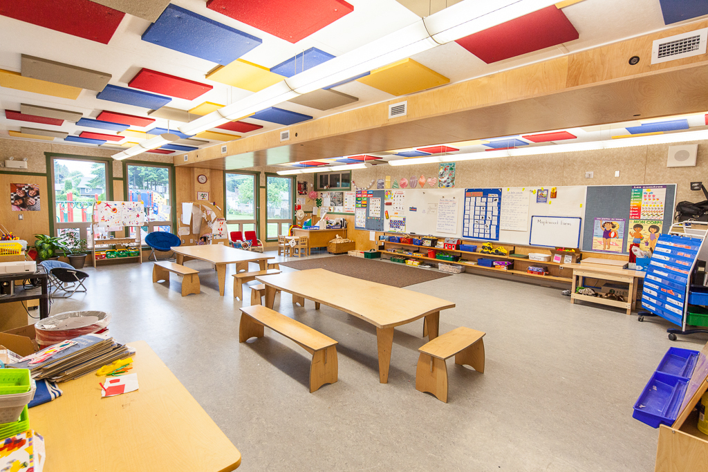全天幼儿园教室显示大量使用木材，包括课桌、椅子、暖通管道镶板、墙镶板和额外的木制品