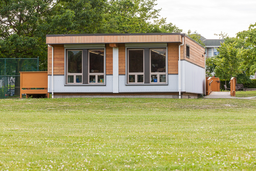 轻型框架低层模块化全天幼儿园教室的外景，展示了完成的模块化单元的混合木材和金属外观