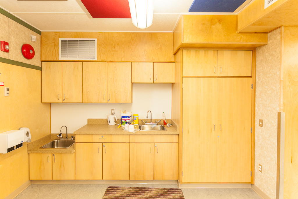 全日幼儿园教室小厨房区域的内部视图，显示木质橱柜和管道