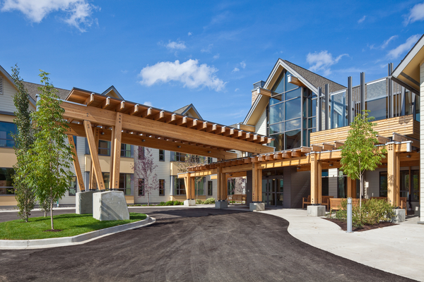 在Gateway Lodge长期护理中心，胶合层压木材(胶合木)和柱子+横梁覆盖的车道入口的外部阳光视图