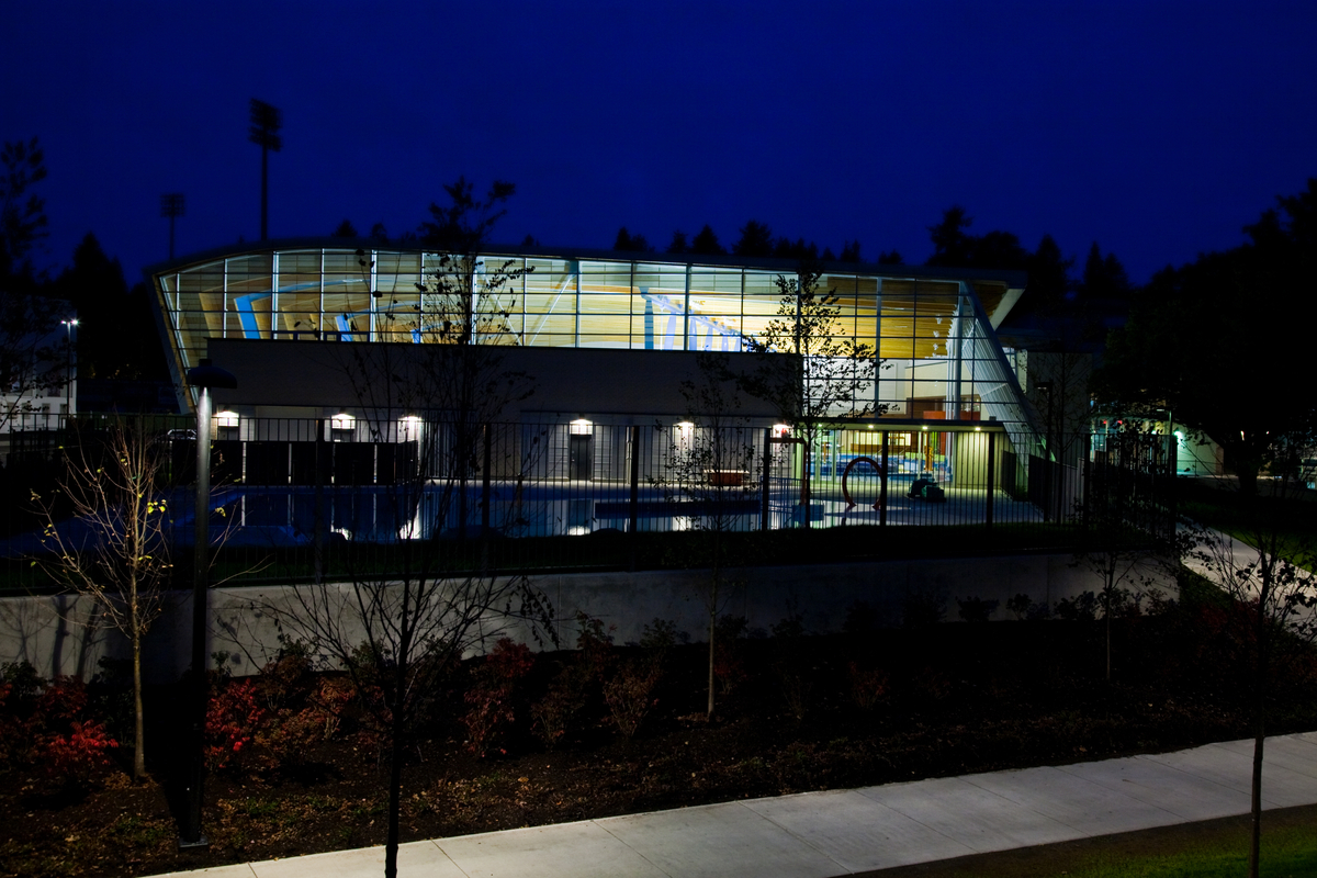 低层建筑Hillcrest Centre的夜间外部图像显示了大面积的玻璃和裸露的木质甲板的天花板，以及内部一系列轻柔弯曲的胶合木梁