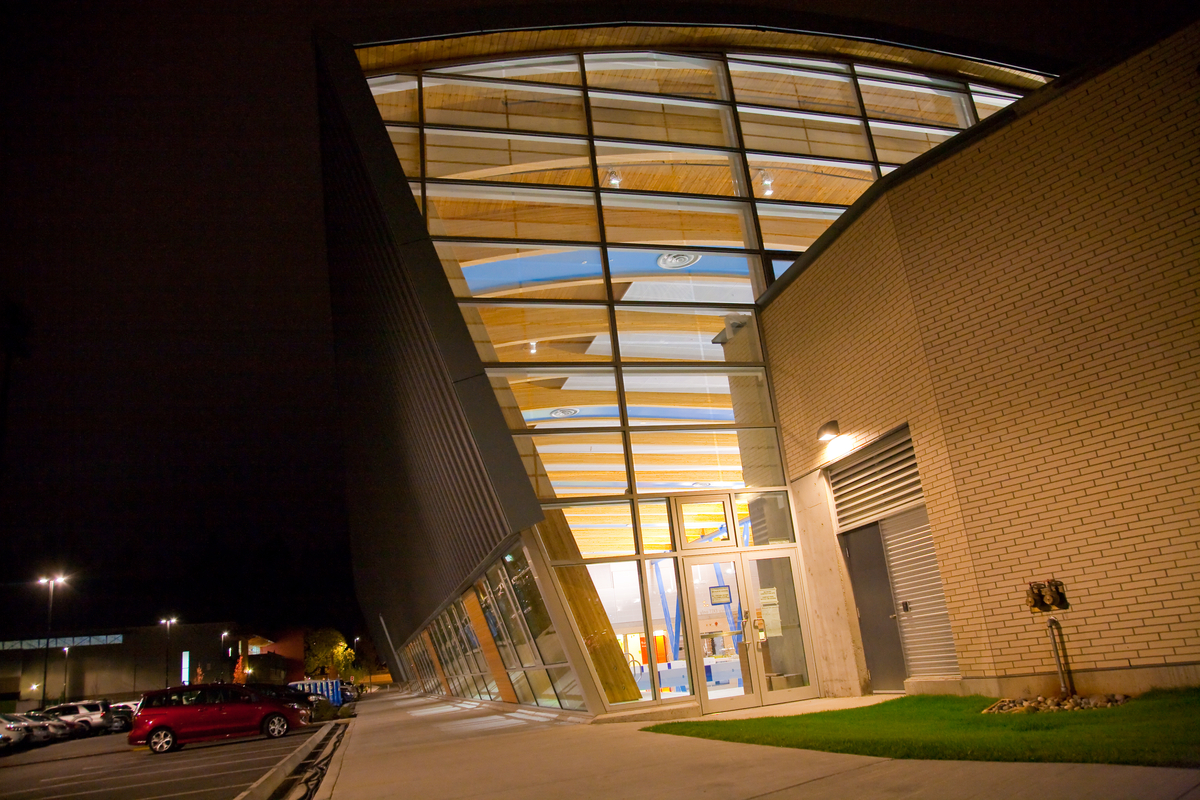 低层建筑Hillcrest Centre的夜间外部图像显示了大面积的玻璃和裸露的木质甲板的天花板，以及内部一系列轻柔弯曲的胶合木梁