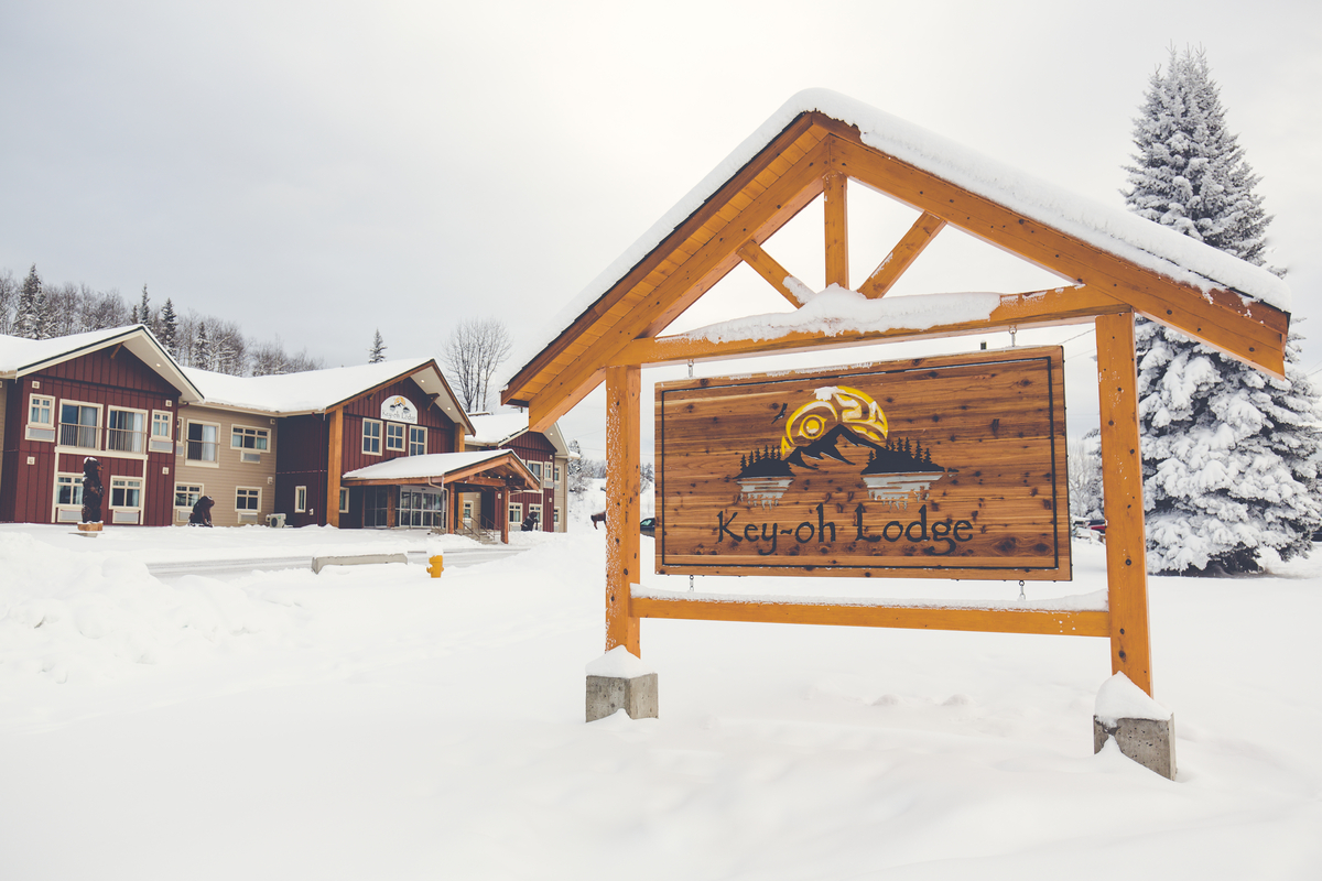 Key-oh Lodge的远处雪景，在前景显示“Key-oh Lodge”木质标识和模块化木材建造的42个房间，在远处的两层精品酒店