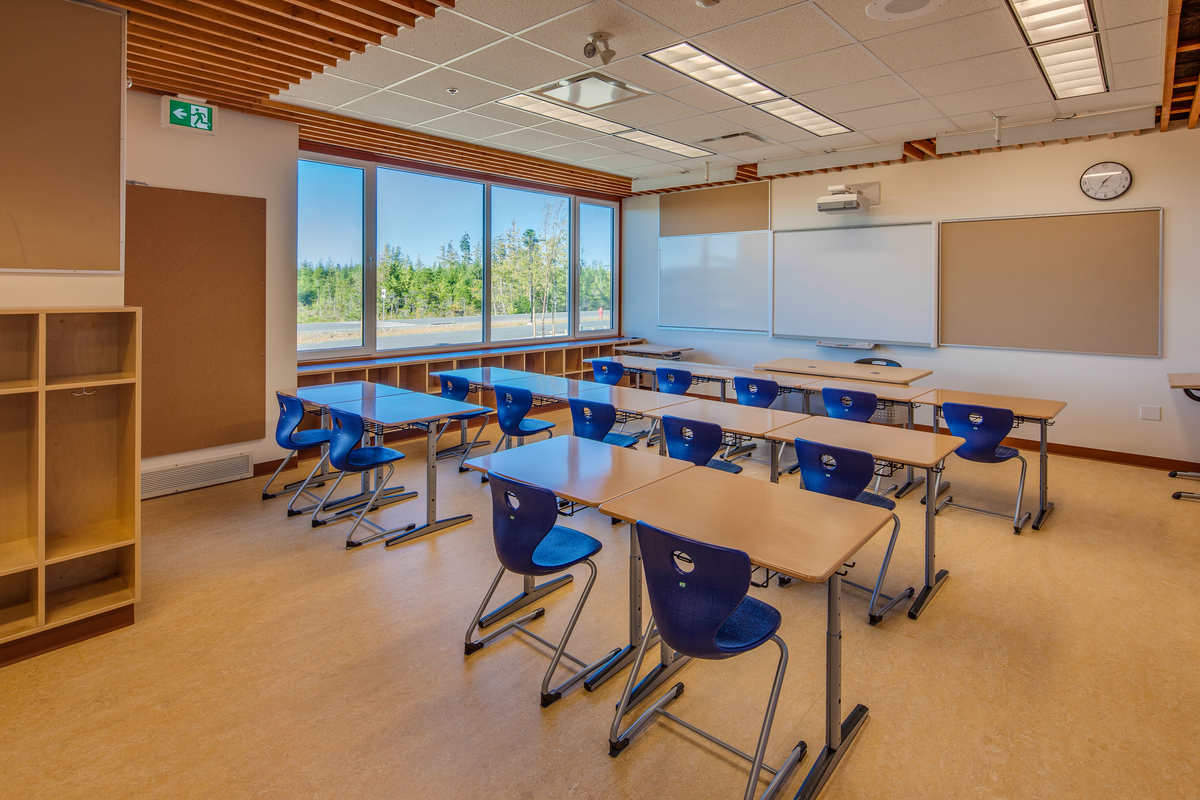 在Kwakiutl Wagalus学校教室的内视图中，木地板、桌面、隔间和混合天花板结构突出