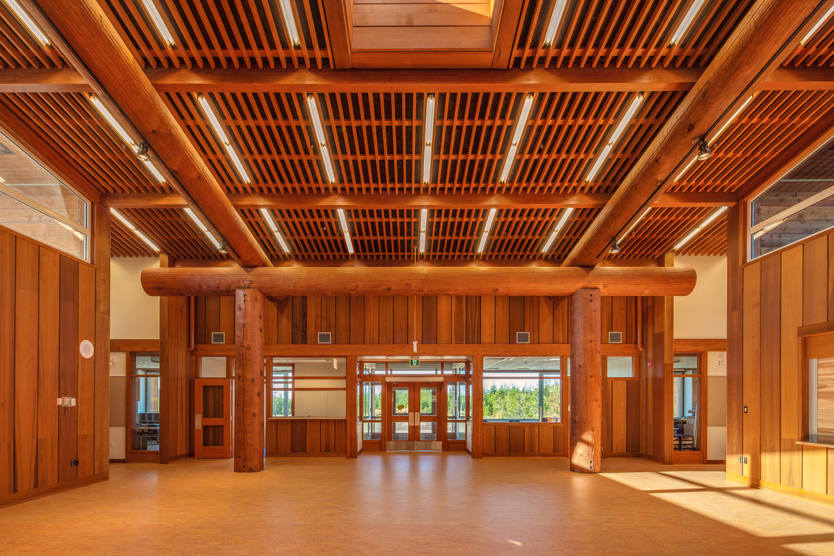 Kwakiutl Wagalus学校阳光明媚的白天室内景观，展示了广泛使用的木材，包括柱、梁和包层的西方红雪松，门和窗户的道格拉斯冷杉，桦木贴面饰面，和枫木硬木运动地板