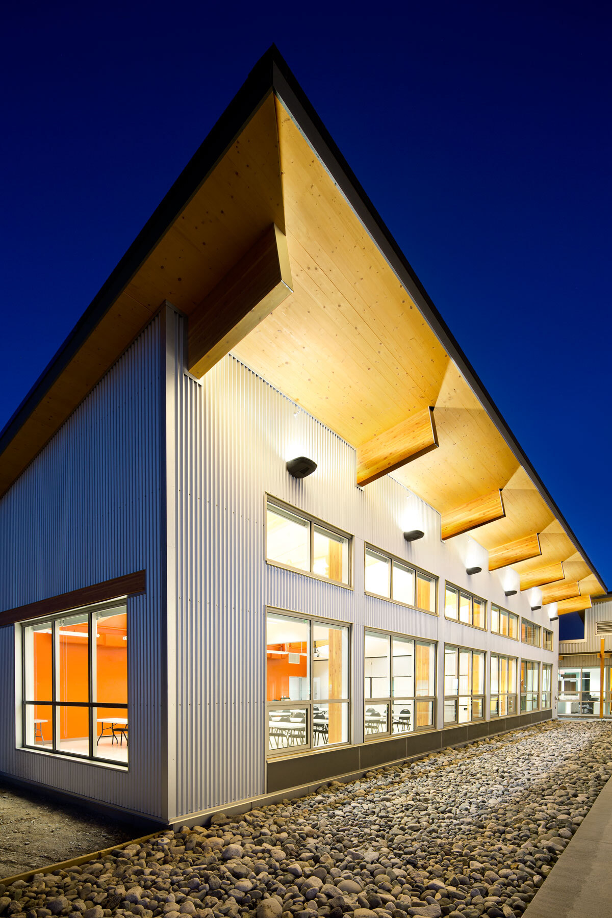 混合低层建筑的外部夜景，梅里特火区办公室和省野火培训中心显示交叉层压木材(CLT)和胶合木(胶合木)梁屋顶延伸到金属包层和玻璃外部