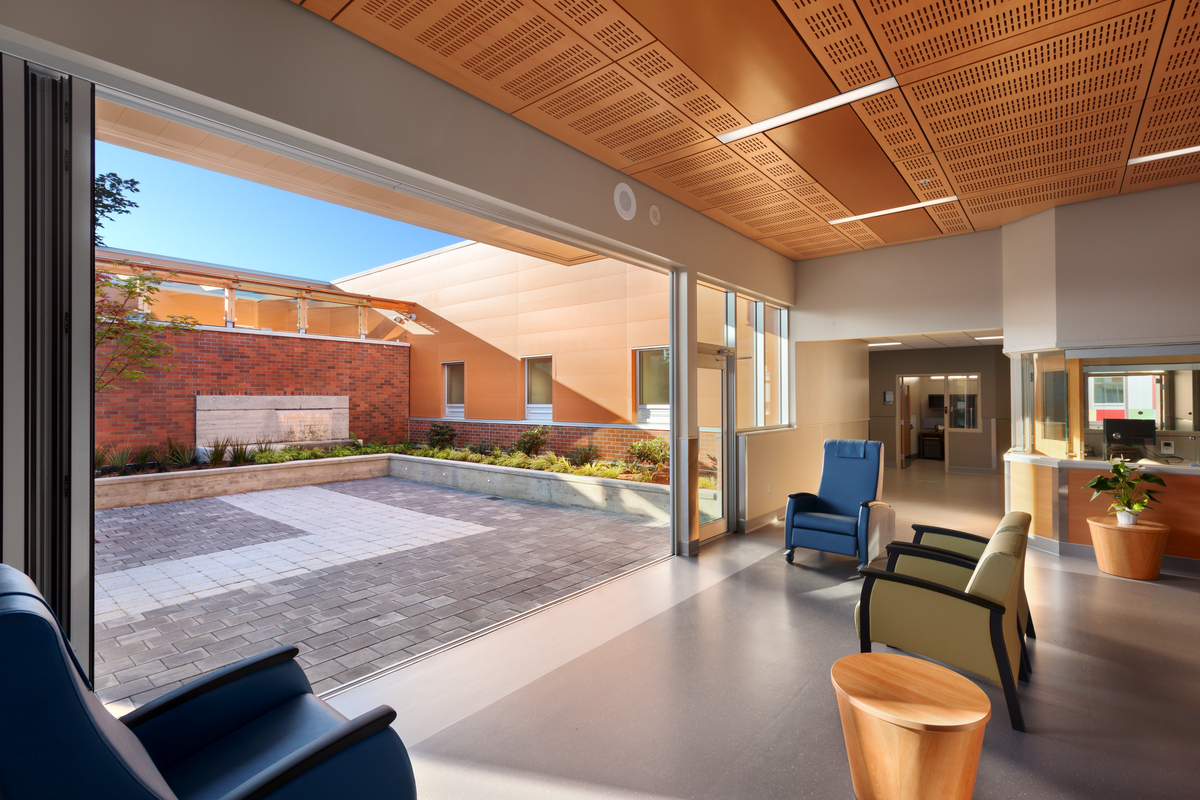 南奈莫地区总医院急诊科入口区域的内部向外视图，显示大开放的入口，外部庭院，大量使用木材，包括建筑内部的木质天花板
