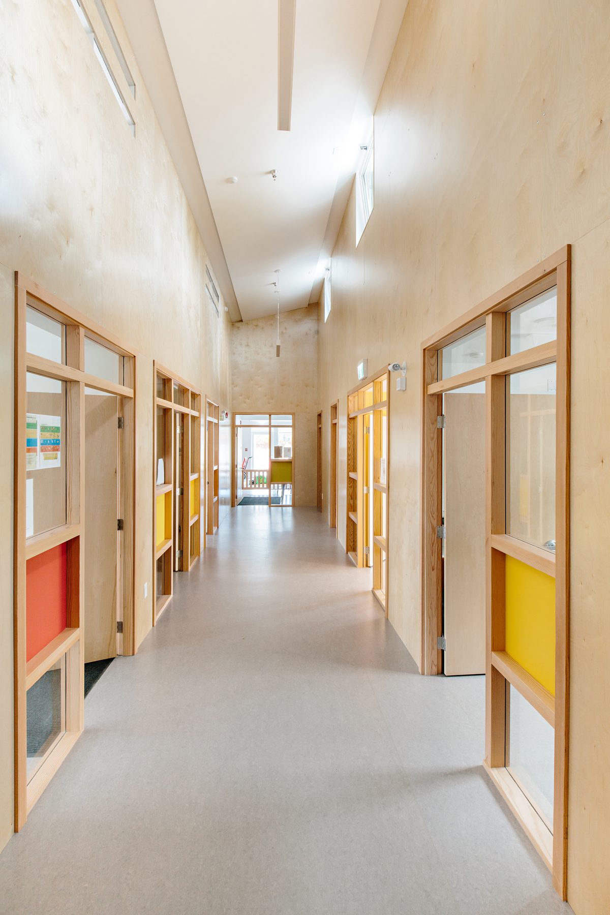 奥卡那根学院幼儿中心低层大厅的室内阳光明媚，展示了木材的广泛使用，包括墙壁、门和装饰