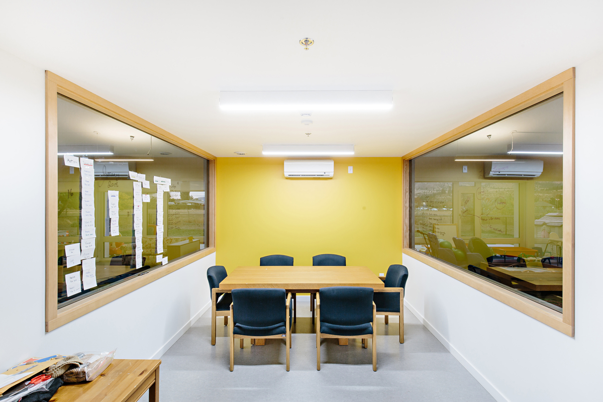 室内阳光明媚的白天景观，奥卡那根学院幼儿中心的低层会议室，六把椅子围绕着一个长方形的桌子，展示了轻框架和大量的木结构，包括木制装饰