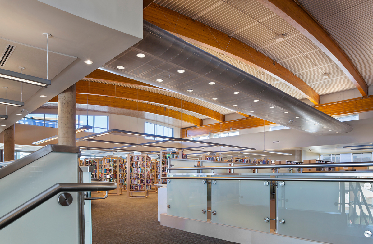 奥卡那根地区图书馆的日间室内景观，展示了大跨度胶合层压(胶合木)屋顶梁，最大限度地减少了对内部柱支撑的需求，以及板条木天花板，以减少环境噪音