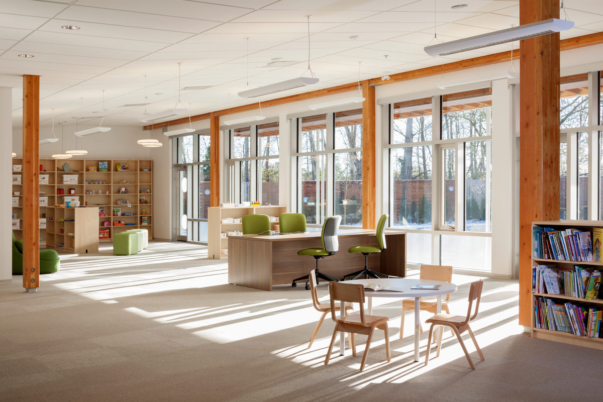 太平洋自闭症家庭中心活动室明亮阳光的室内景观，展示了外部玻璃窗和室内木材，其中包括胶合木(胶合木)梁和柱，木橱柜和木装饰