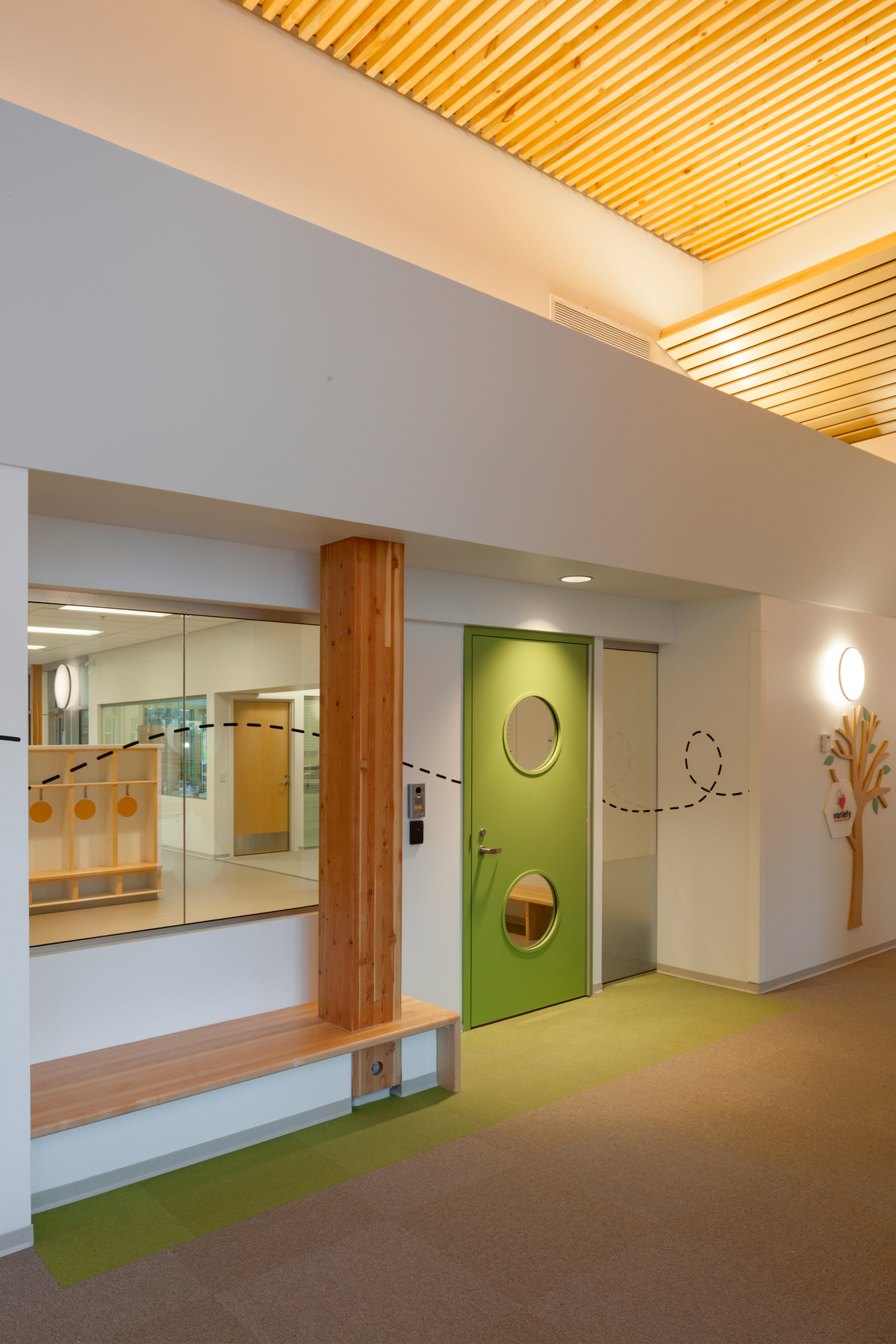 太平洋自闭症家庭中心明亮阳光的室内景观，展示了彩色的绿色室内门附近的胶合木(胶合木)柱支撑着上面的尺寸木材板条天花板
