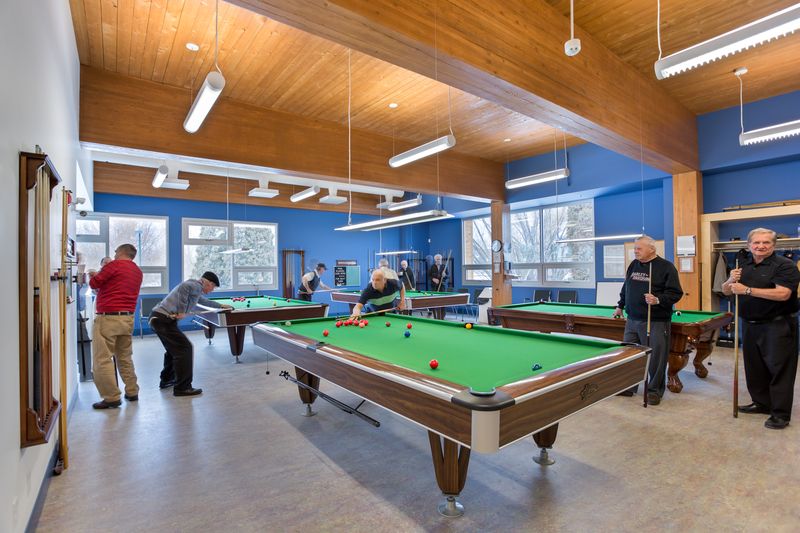 帕金森活动中心的内部，人们在一个光线充足的房间里社交和打台球，房间里有大木梁和木制天花板