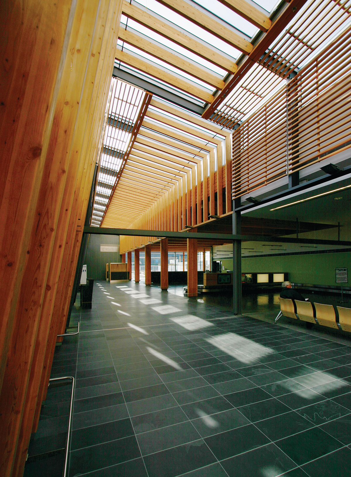 乔治王子机场扩建低层建筑的室内日间景观，显示胶合木梁和柱与艺术尺寸的木材板条混合