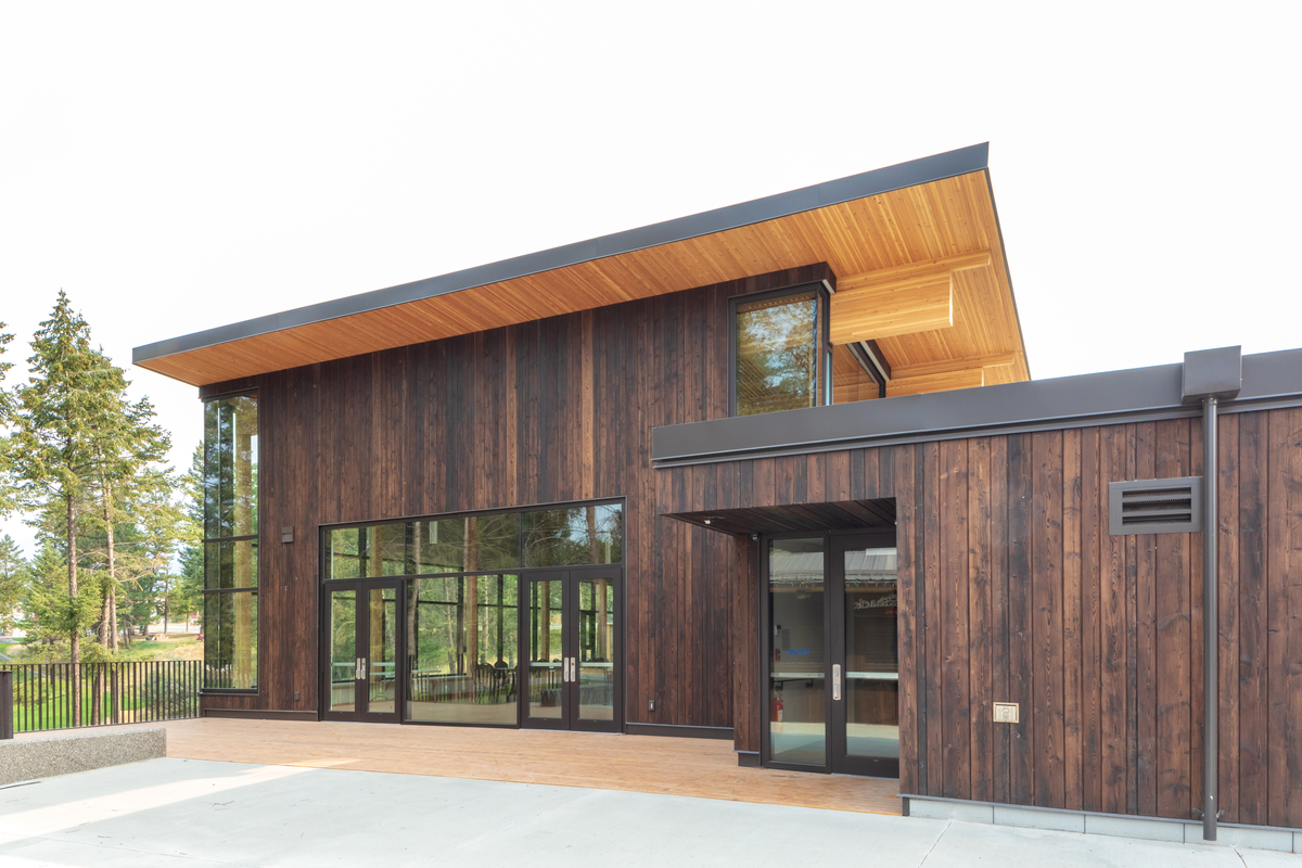 白天阴天的镭温泉社区会堂和图书馆低层建筑的外景，显示深色木镶板和榫压木(DLT)和胶合木(胶合木)屋顶木材