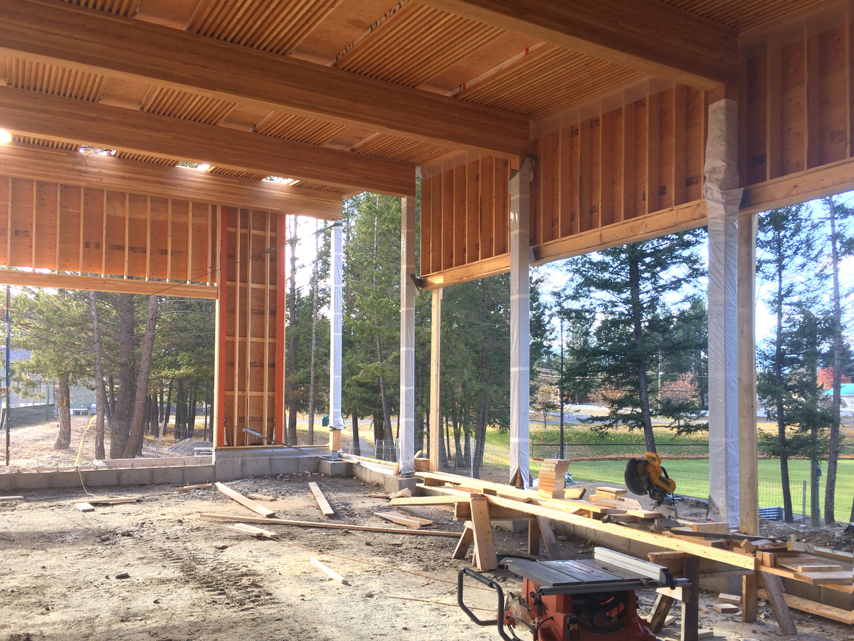 正在建设中的镭温泉社区大厅和图书馆的日间外观，展示了榫压木(DLT)梁，轻型框架墙，和大量的木柱