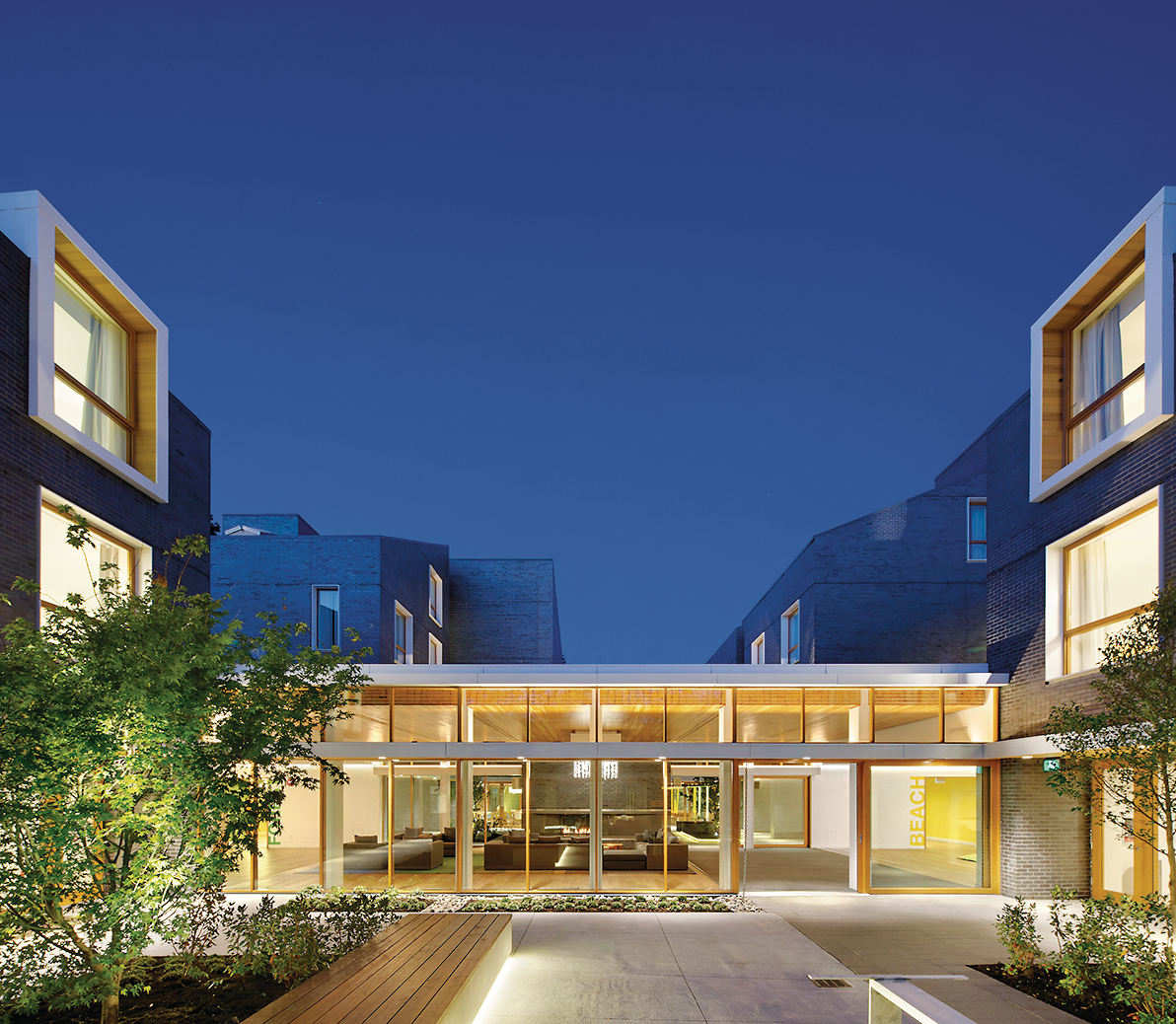 育空BC罗纳德麦克唐纳住宅的外部夜景，展示了大型外部庭院，通过玻璃可以看到公共区域，完成了裸露的木地板和天花板