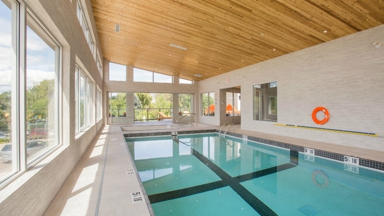 Sandman Signature Kamloops酒店游泳池的日间室内景观，展示了多维度的木材板条屋顶和大窗户