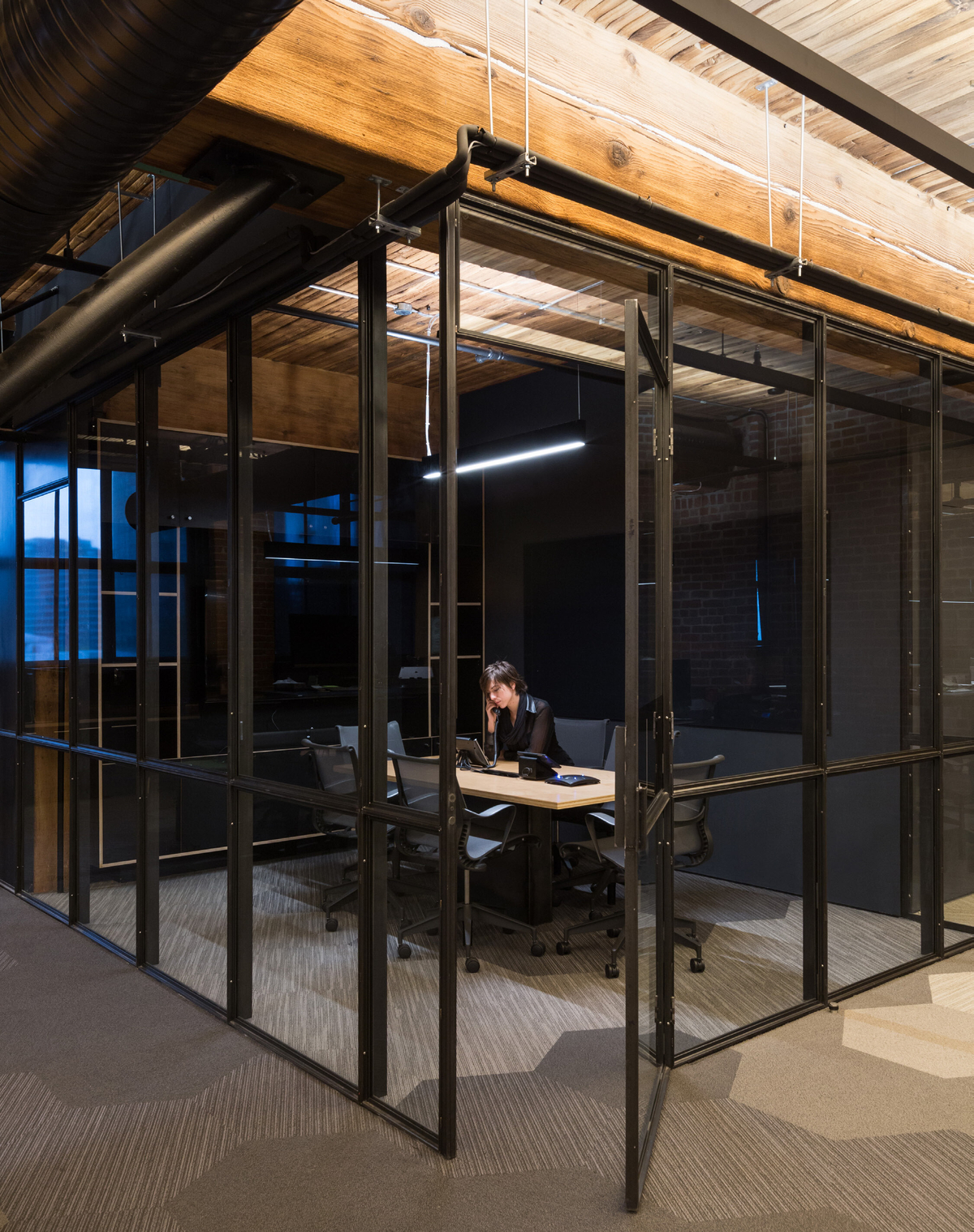 Slack总部的内部夜景，展示了有百年历史的木结构柱和梁结构，在现代玻璃办公室和技术工人的上方是木质天花板