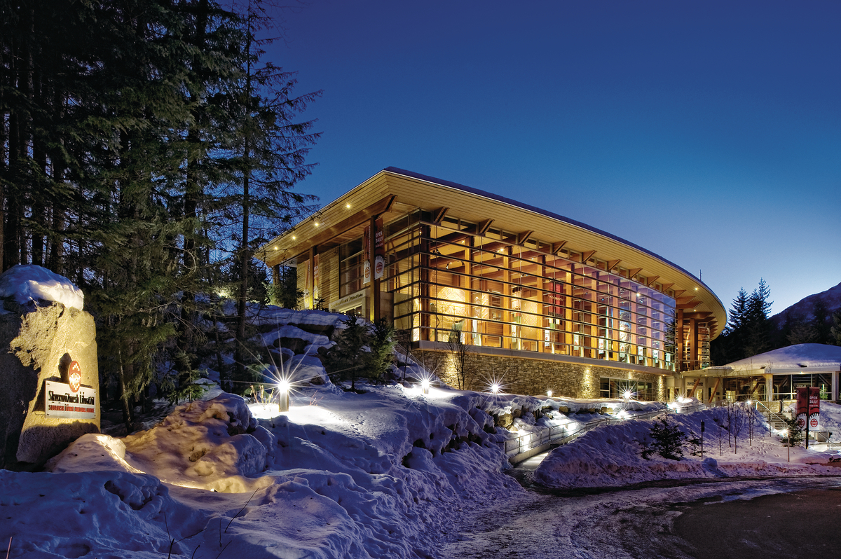 低层建筑Squamish Lilwat文化中心的雪景夜景，展示了弧形玻璃、胶合木(胶合木)和柱+梁木材元素