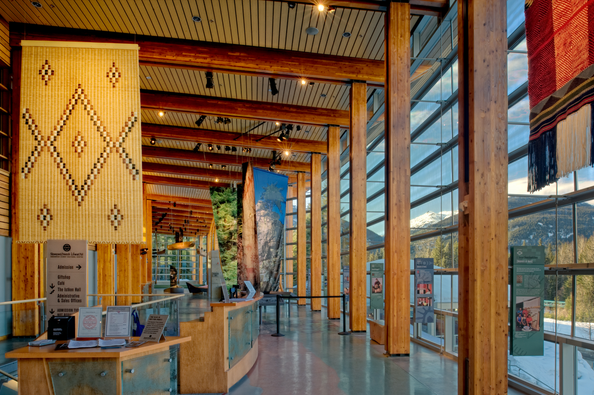 Squamish Lilwat文化中心的日间室内景观突出了木地板、手工编织的垫子，以及柱子、阳台和天花板结构中大量使用的木材