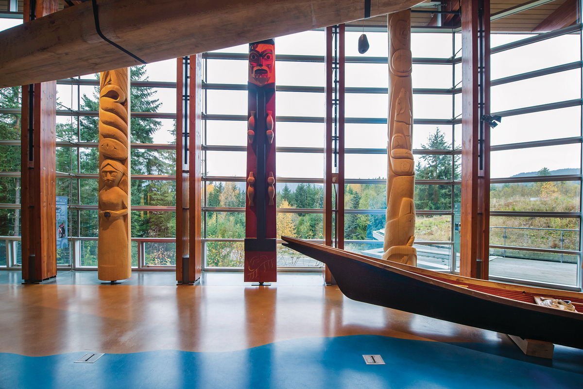Squamish Lilwat文化中心的室内日间景观，突出木地板，雕刻木独木舟，和复杂雕刻的第一民族垂直木柱