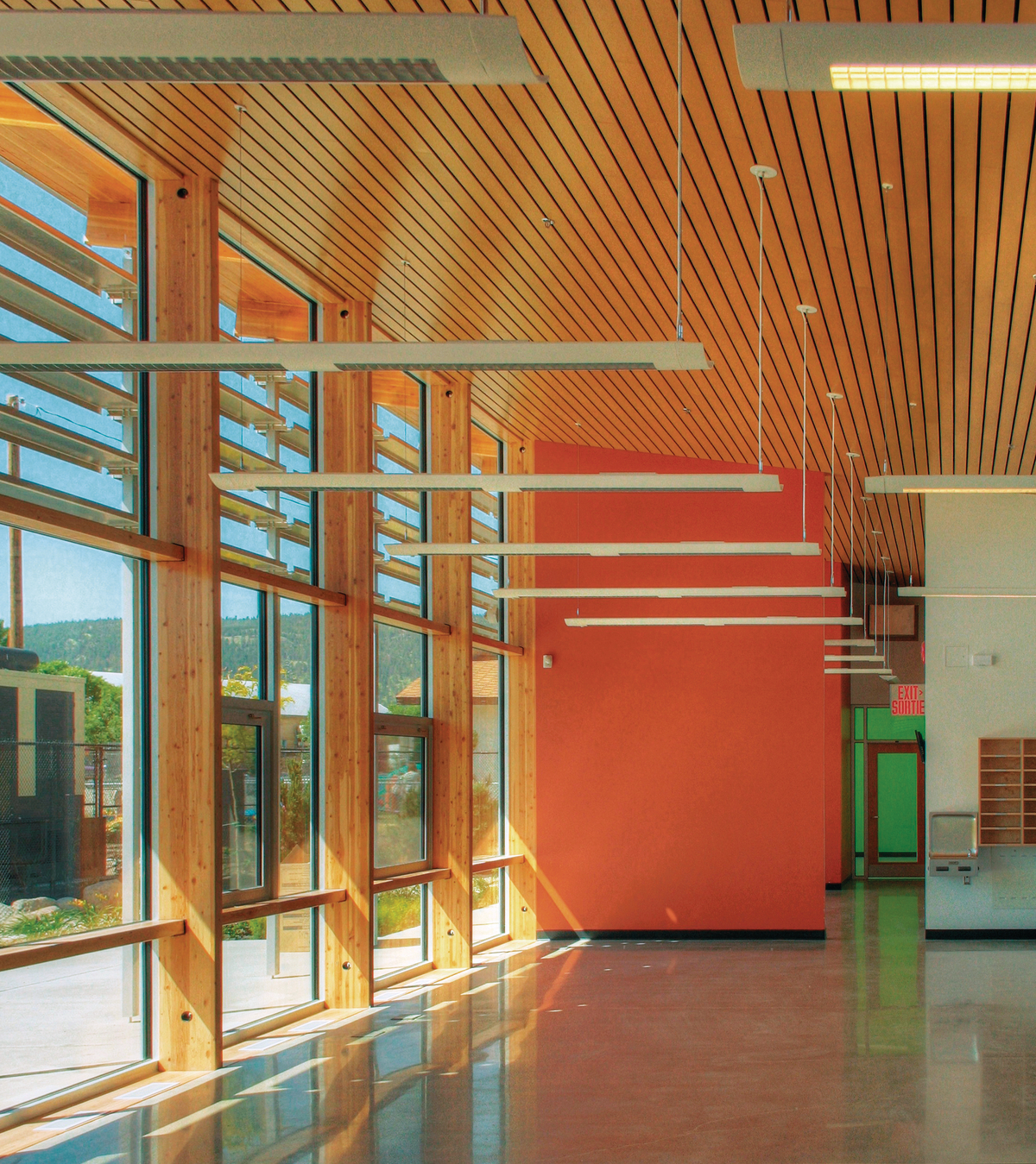 室内阳光明媚的白天景观突出了垂直块状木柱的使用，以及木装饰和装饰尺寸的木材天花板，位于新完成的Summerland RCMP支队内