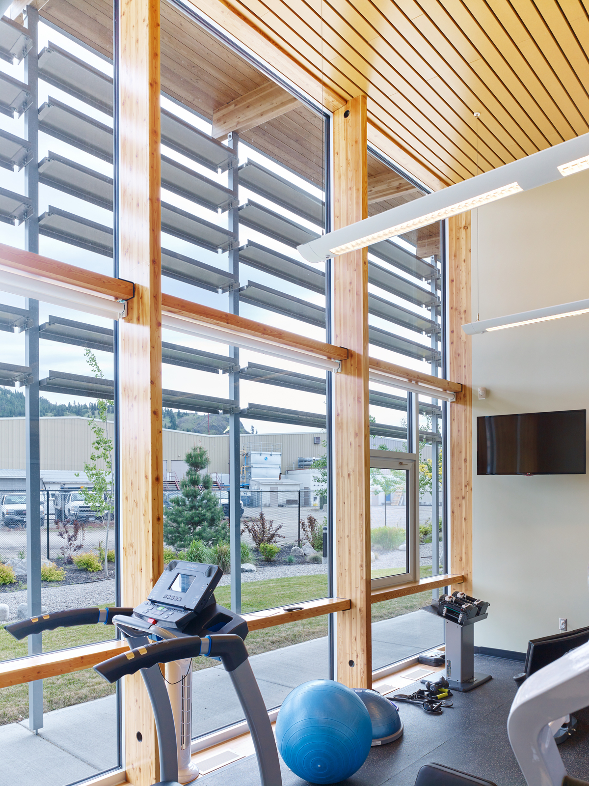 室内阳光充足的白天景观突出使用垂直体量的木柱和装饰尺寸的木材天花板在Summerland RCMP支队锻炼室内