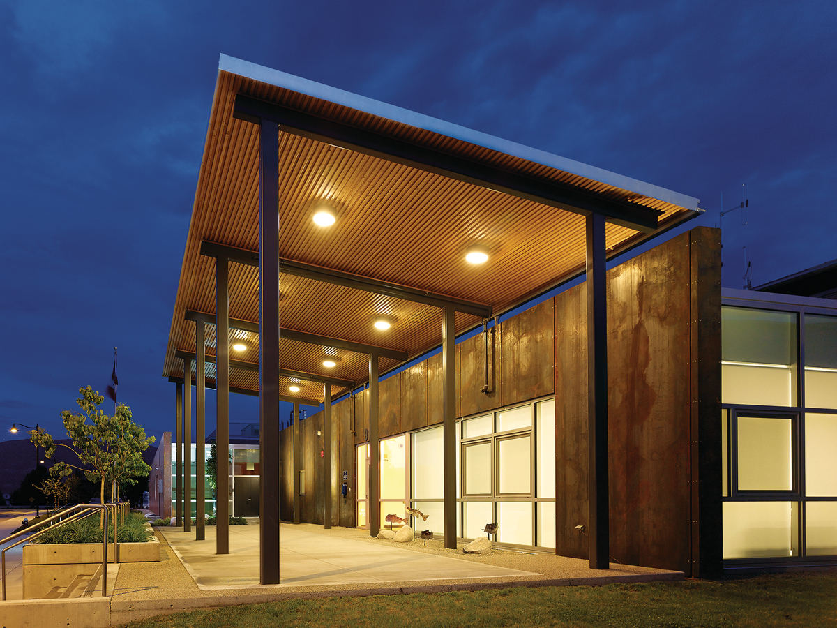低层建筑Summerland RCMP支队的阴天夜景，显示外部有覆盖的走道，混合木材和金属结构，底部覆盖未完成的松木板