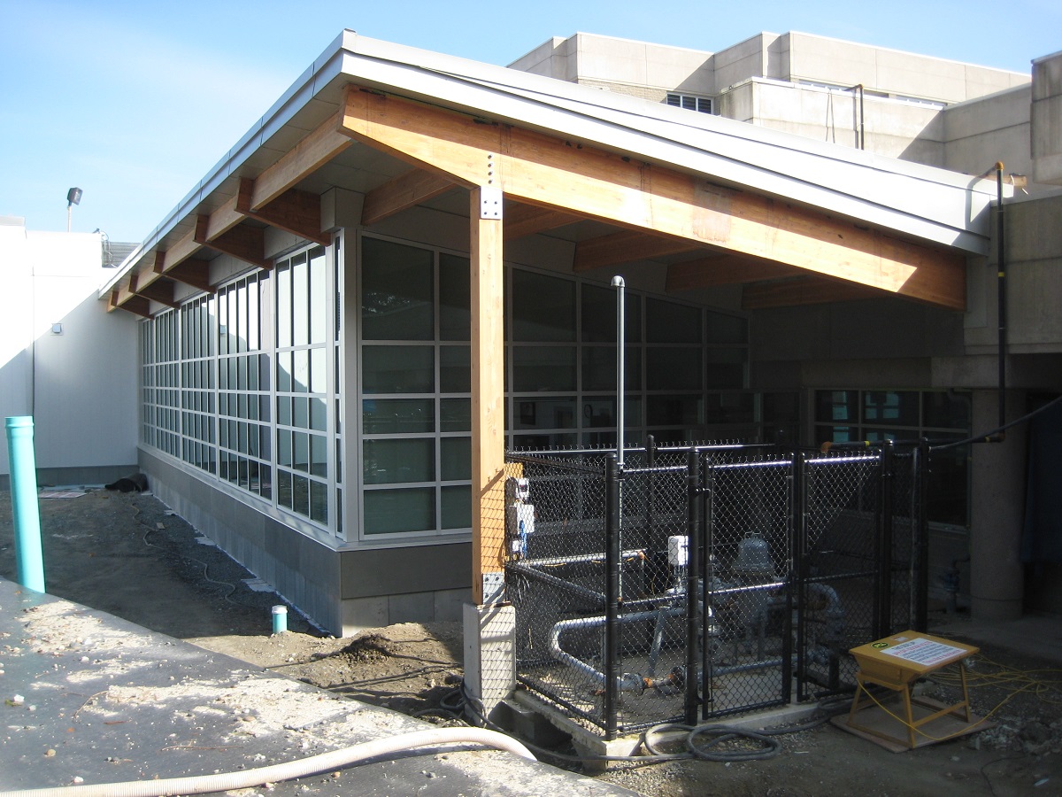 萨里预审服务中心单层部分的白天特写，外部阳光充足，展示了金属、玻璃和木材混合元素，包括由胶合层压木材(胶合木)梁和柱支撑的屋顶