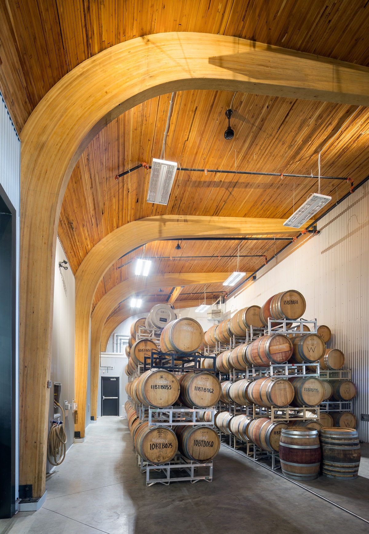 在时代酒庄的酒桶储藏室里，胶合层压木材(胶合木)形成了弯曲的柱/梁，支撑着交叉层压木材(CLT)的天花板