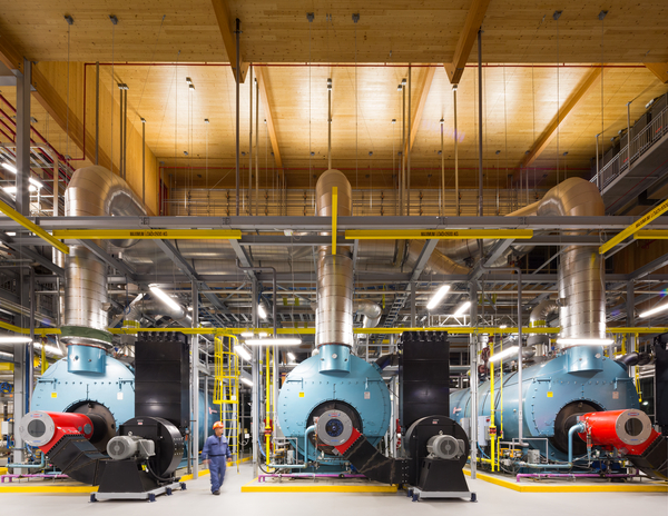 UBC校园能源中心的内部图像显示了三个大型锅炉，一个穿着工作服的工人，以及大量胶合层压木材(胶合木)的柱子和梁框架，以及交叉层压木材(CLT)封闭的墙壁和屋顶